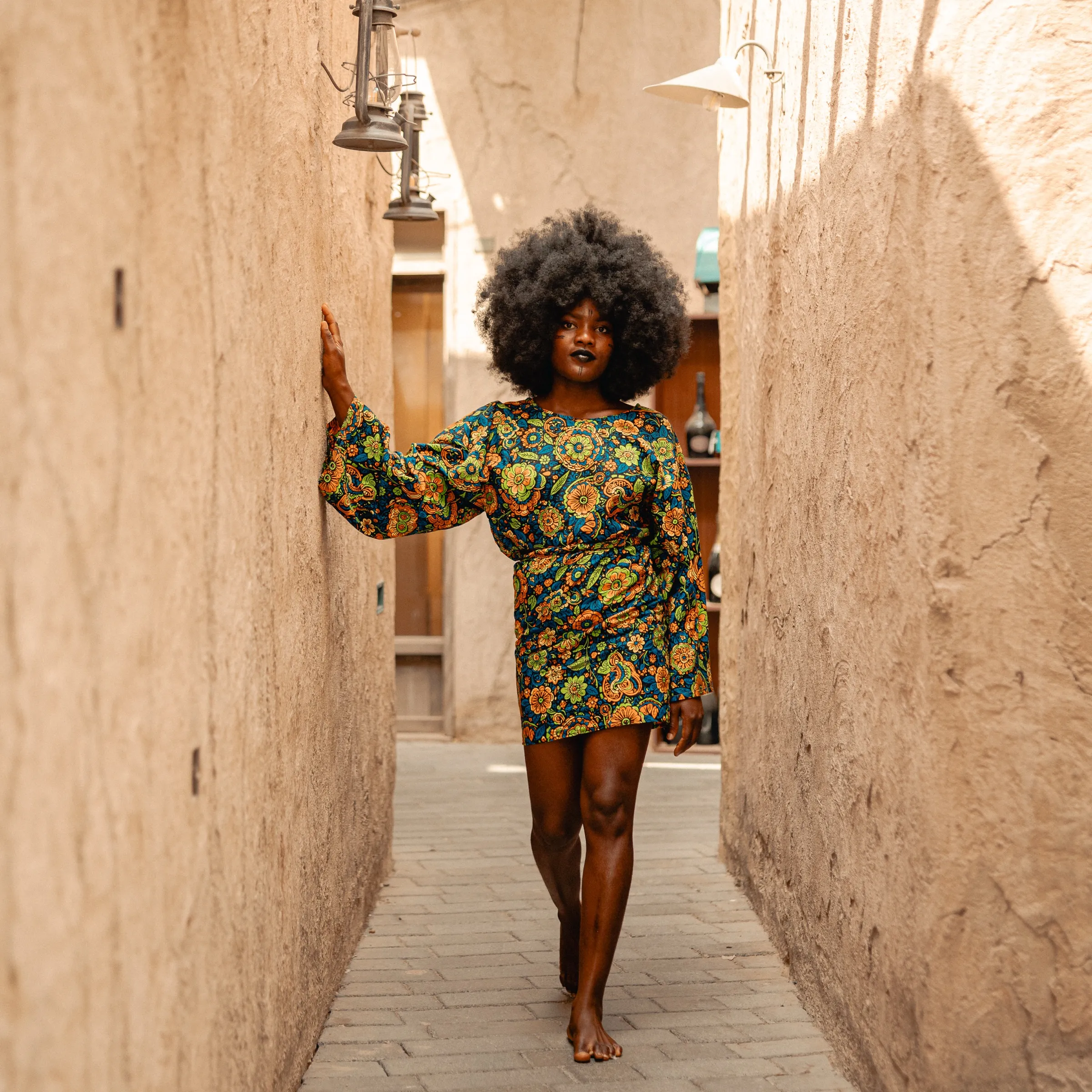 A model in a bold print dress posed in a sandstone alleyway