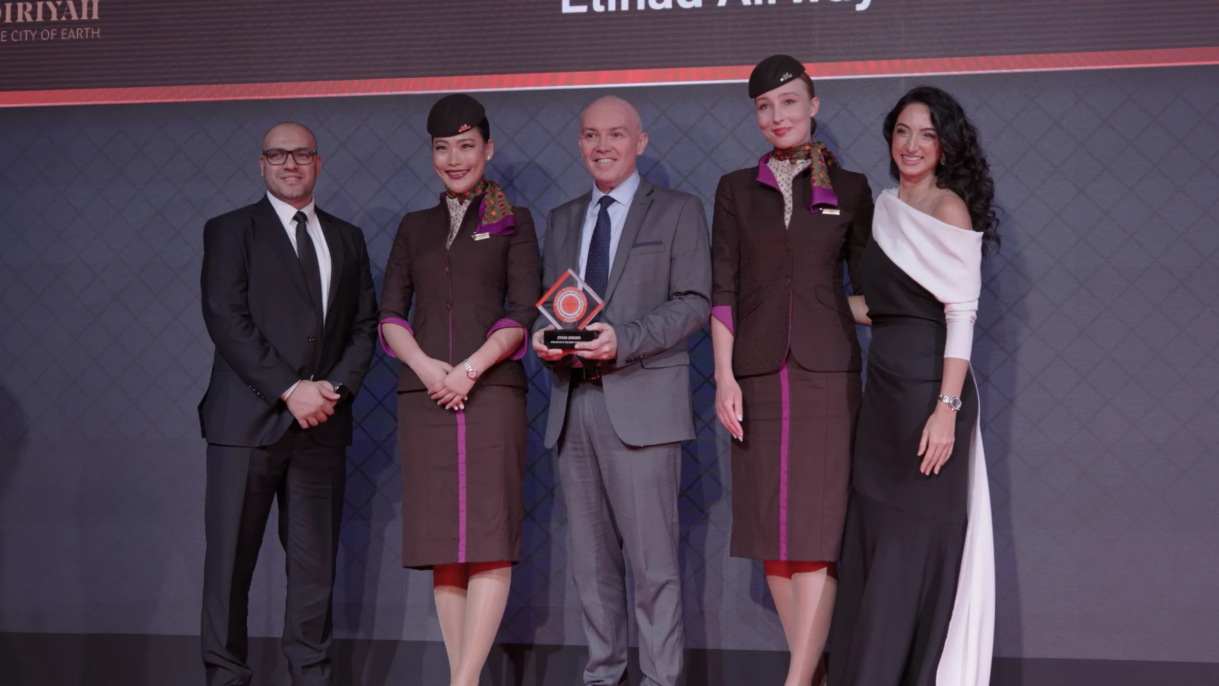 Award winners in uniform receiving a trophy on stage in front of a branded backdrop