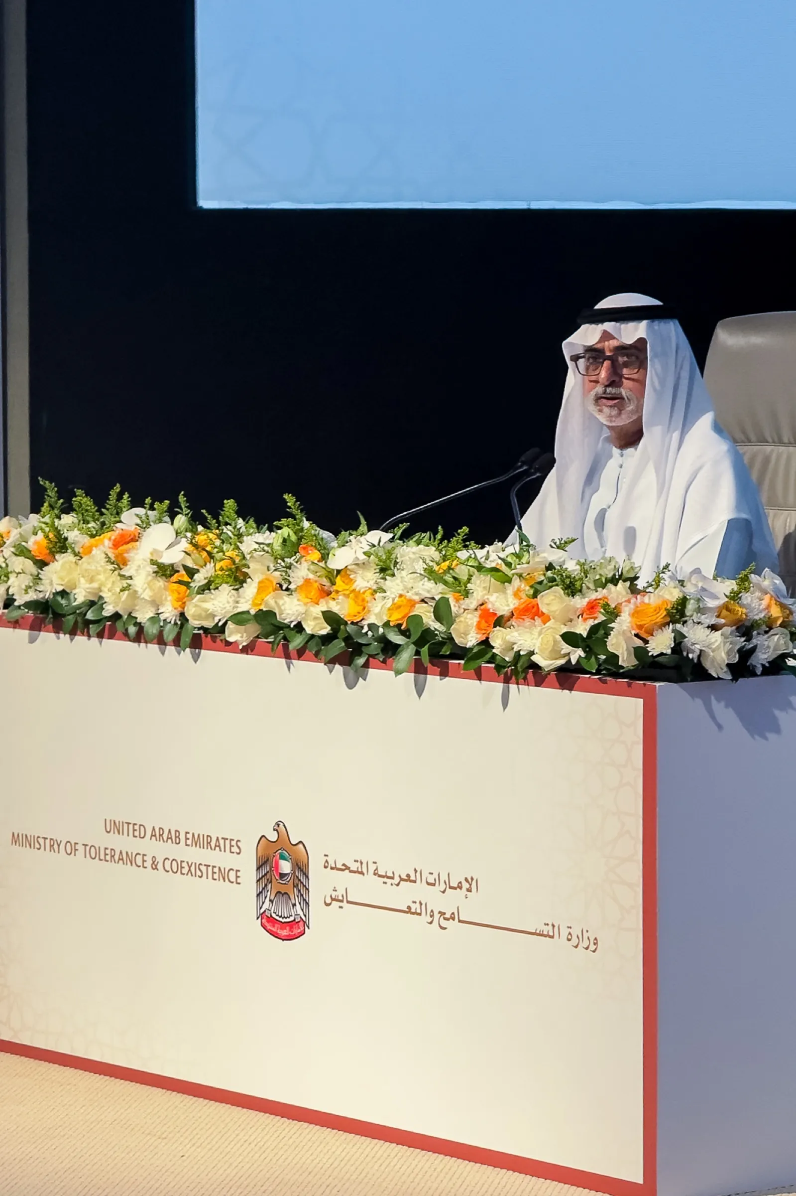 A speaker at a flower-banked podium during a UAE government forum