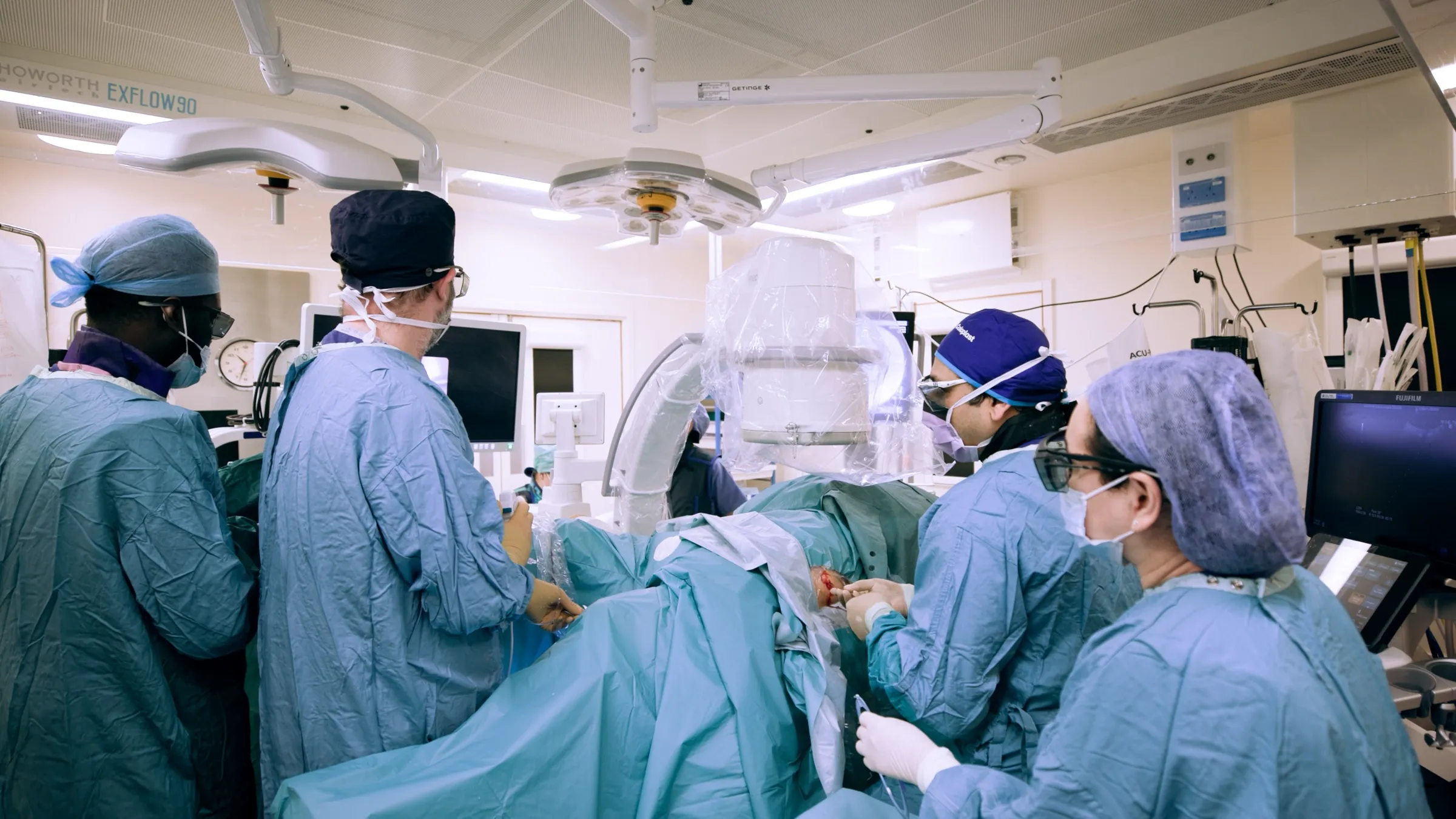 A surgical team operating in a theatre under overhead lights, filmed for a medical device client
